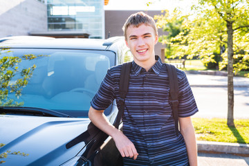 Happy male teenager leaning against his car in a high school parking lot.