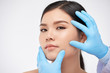 © DragonImages - Gloved hands of cosmetologist examining flawless face of beautiful young woman