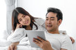 © nuiiko - Happy Asian couple using laptop and tablet together on bed at home, lifestyle concept.