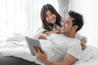 © nuiiko - Happy Asian couple using laptop and tablet together on bed at home, lifestyle concept.