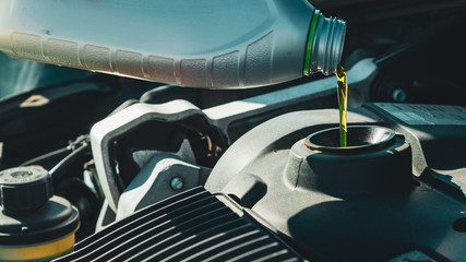 Process of adding oil to the engine, man checking his car before driving, thick yellow liquid is poured into a special hole, technical inspection of the motor