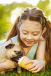 Little girl kid feeding pug dog on summer day