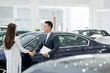 © DragonImages - Smiling salesman and pretty female client shaking hands in car showroom