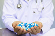© PhotoJuthamat - Healthcare and medical concept . Doctor in uniform holding white and blue capsule pill in office at hospital,Selective focus