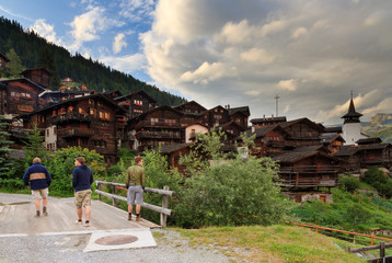 Wall Mural - Tourists walk through the beautiful alpine village Grimentz, Switzerland, with traditional wooden houses and church tower in summer 