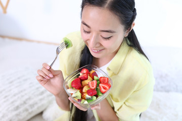 Asian woman eating healthy fruit salad at home