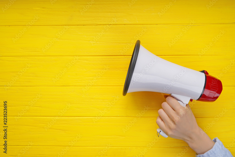 Woman holding megaphone on color wooden background