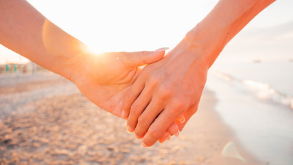 Close up of two female holding hands against sunset - two girls walking on the beach hand by hand - same-sex lesbian couple and female friendship concepts