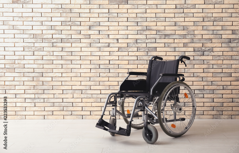 Empty modern wheelchair near brick wall indoors