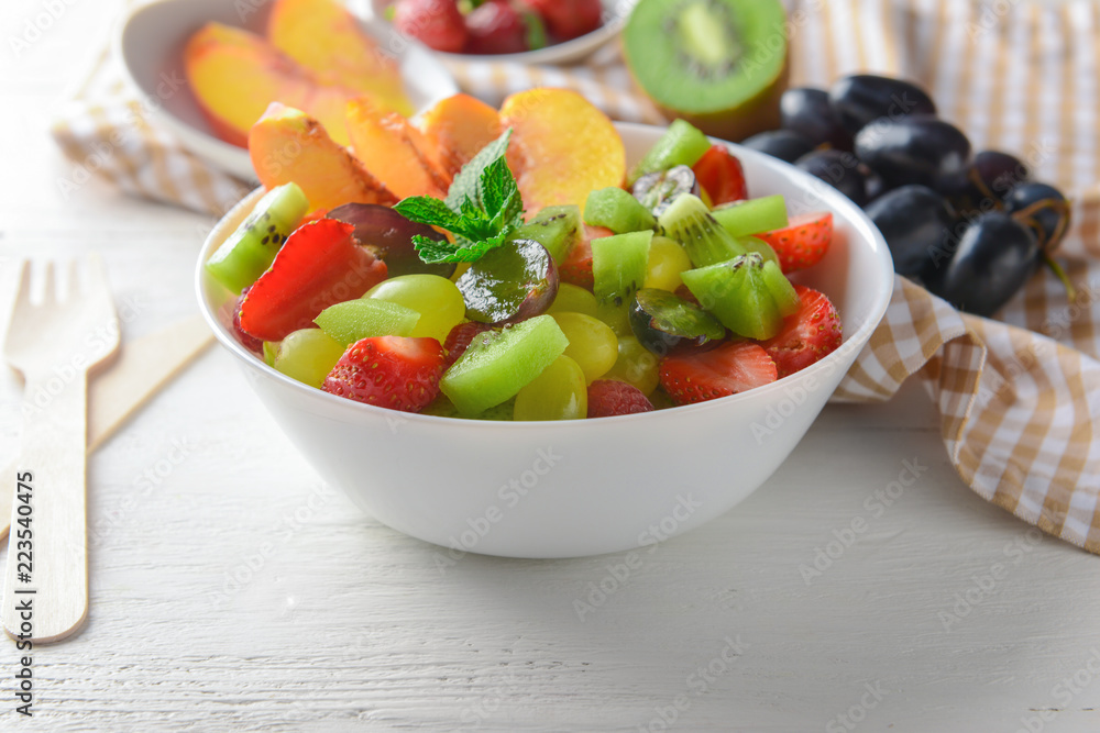 Bowl with delicious fruit salad on white wooden table