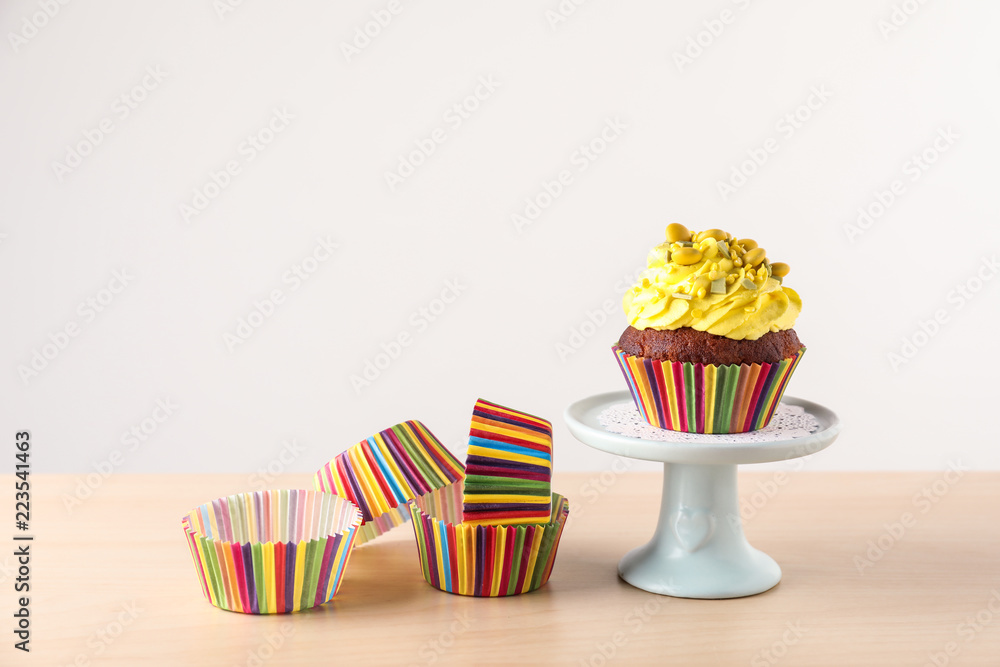 Dessert stand with delicious cupcake and baking cups on light wooden table