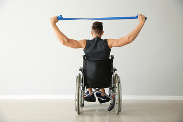 Poster - Sporty man training with elastic band while sitting in wheelchair against light wall