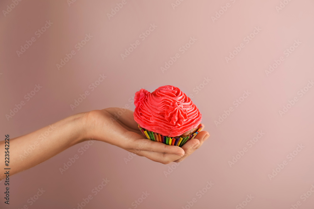 Woman holding tasty cupcake on color background