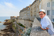 © dennisvdwater - Tourist enjoys the ocean view from the wall of the historic city Saint-Malo in Brittany, France, a major summer vacation tourist destination