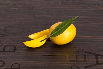 Wall Mural - A Mango with leaf and stem and some cut slices of mango on brown background