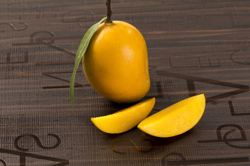 Wall Mural - A Mango with leaf and stem and some cut slices of mango on brown background