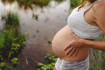 Wall Mural - Close-up of pregnant woman's belly stroking with her hands in nature.