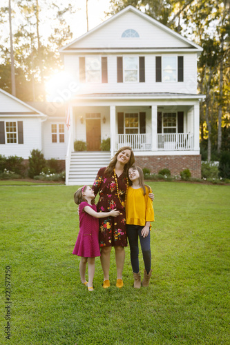 Fotografie, Obraz Mom and Two Daughters Laughing and Hugging Outside their New Farmhouse Home