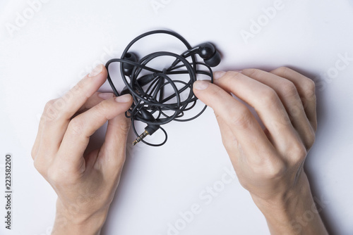 Fotografie, Obraz Female hands unravel the black little headphones on a white background
