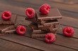 A stack of chocolate bars with built-in red raspberry berries. Fresh raspberries and chocolate on wooden background.