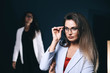 © velimir - two beautiful sexy business women in in a jacket and glasses in the studio on a dark background. colleagues, partners - team.