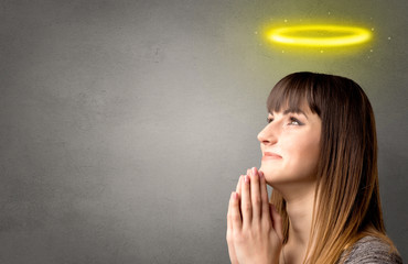 Young woman praying on a grey background with a shiny yellow halo above her head