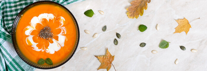 Wall Mural - Delicate pumpkin puree with cream and chia seeds in a black glass bowl on a light background. Top view. Banner.