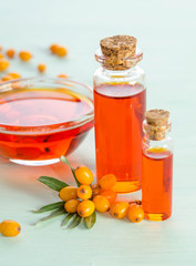 Wall Mural - Sea buckthorn and two bottles, bowl  with sea buckthorn oil on blue table