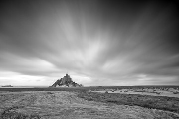 Wall Mural - Beautiful view of historic landmark Le Mont Saint-Michel in Normandy, France, a famous UNESCO world heritage site and tourist attraction, long exposure with ominous clouds in black and white