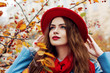 © Victoria Fox - Close up outdoor portrait of young beautiful happy smiling girl wearing red hat and scarf posing near autumn tree. Model with red lips, long hair. Lady looking up.