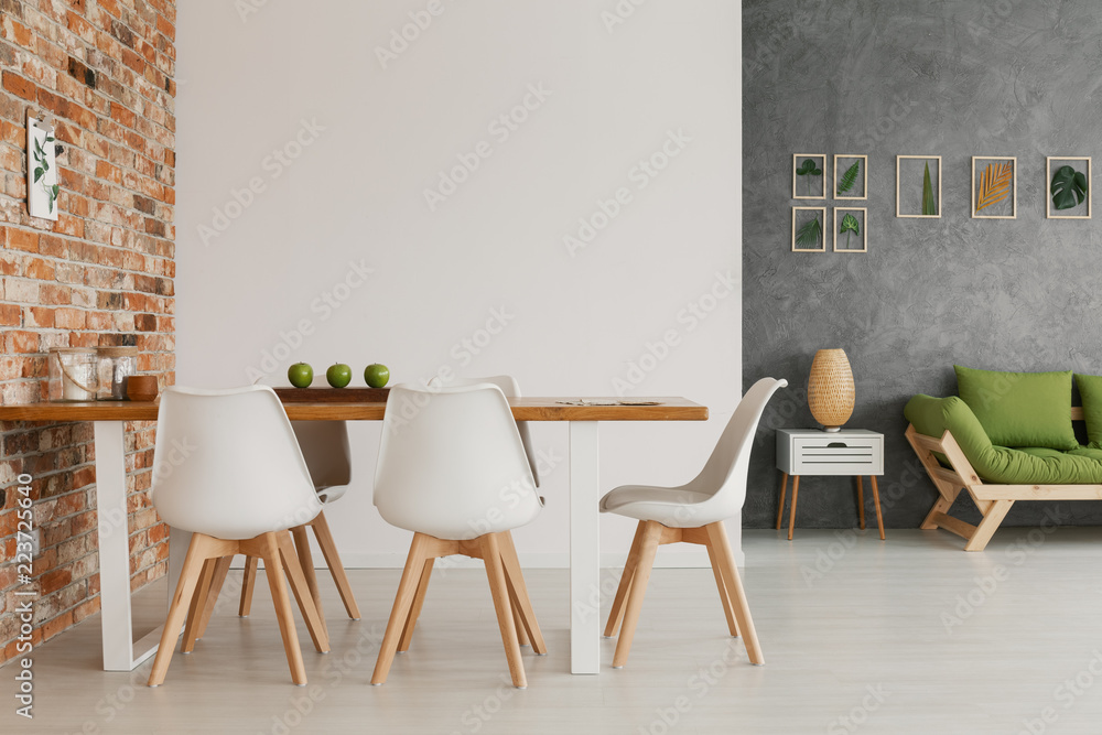 Wooden dining table and chairs by an exposed brick wall in a bright and natural living room interior of a modern loft - obrazy, fototapety, plakaty 