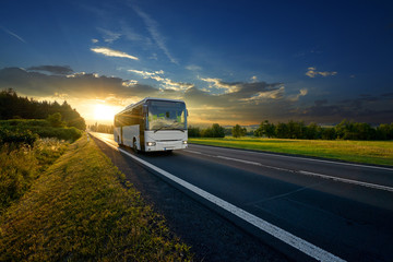 Wall Mural - white bus arriving on the asphalt road in rural landscape in the rays of the sunset