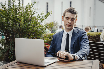 Close up of businessman holding mobile phone in hand and looking at watches.