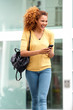 © mimagephotos - happy young woman walking in the city with mobile phone and bag