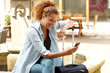 © mimagephotos - happy young woman sitting with suitcase and looking at mobile phone