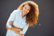 © mimagephotos - happy young woman smiling with arms crossed by gray wall