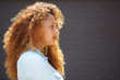 © mimagephotos - Profile young woman with curly hair against gray wall