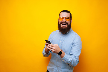 Cheerful bearded man with yellow sunglasses using smartphone and smiling