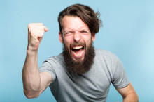 Victory Success And Achievement. Excited Thrilled Agitated Guy Making A Win Gesture. Hipster Man Portrait On Blue Background. Emotional Reaction And Facial Expression Concept.
