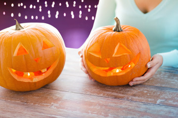 Wall Mural - halloween, decoration and holidays concept - close up of woman with carved pumpkins over ultra violet background