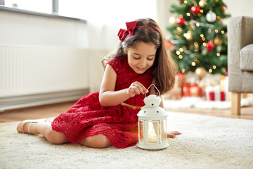 christmas, holidays and childhood concept - happy little girl playing with lantern at home