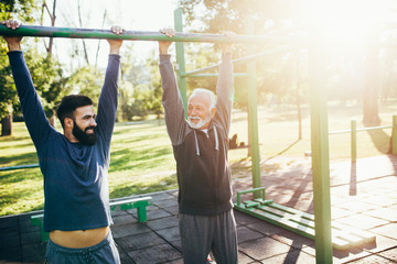 Happy good looking father and son exercising together in park.