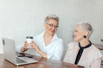 Two business women sitting at table in coffee shop, look at laptop. table laptop and cup of coffee