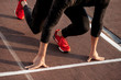 young man wearing black clothes and red shoes in starting position for running on sports track in stadium