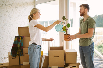 Smiling couple unpack boxes in new home. Woman giving flower to her husband