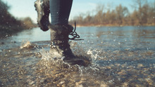 LOW ANGLE, DOF: Girl In Black Waterproof Boots Splashing The Clear Lake Water.