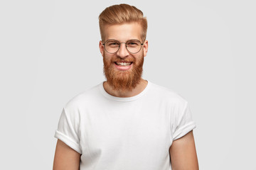 photo of attractive ginger man with satisfied expression, has thick beard, rejoices promotion at wor