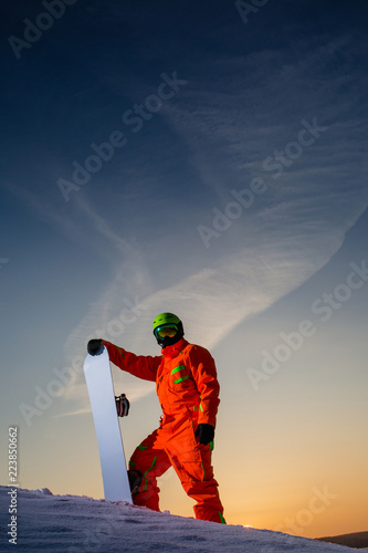 Fototapeta na szkło Snowboardzista na szczycie stoku narciarskiego na tle pięknego zachodu słońca