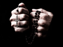 Female Hands Praying Holding A Rosary With Jesus Christ In The Cross Or Crucifix On Black Background. Woman With Christian Catholic Religious Faith