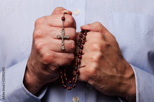 Cuadros en Lienzo Male hands praying holding a beads rosary with Jesus Christ in the cross or Crucifix on black background